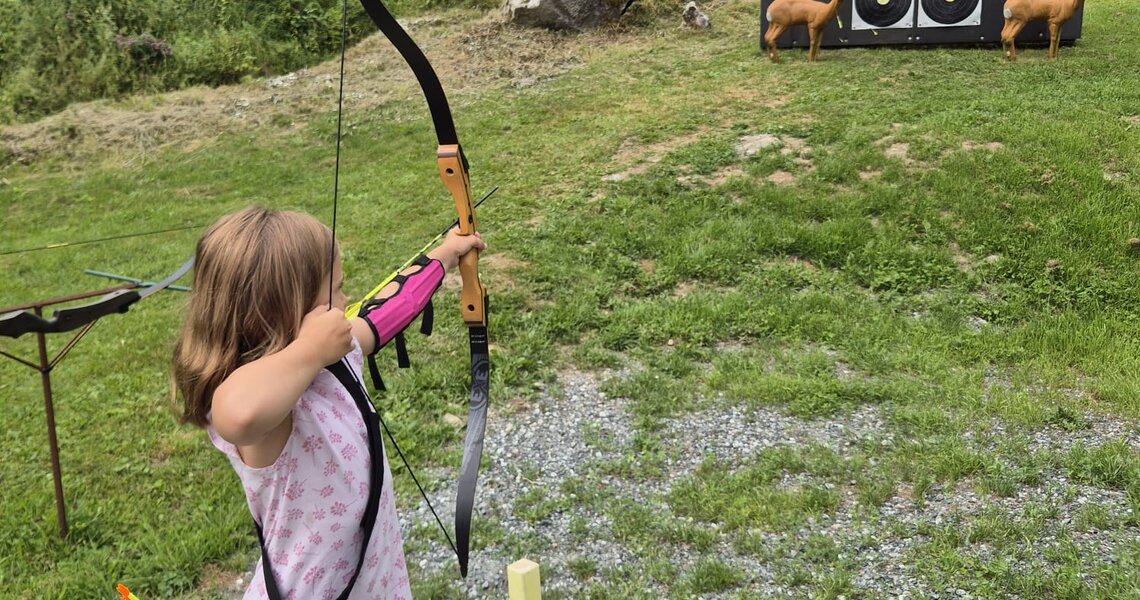 Child practicing archery on a meadow with targets in the background. | © Bogensport Vorderegger