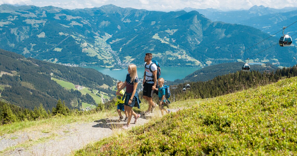 Family hiking on a mountain with view of lake, valley and cable car in background. | © Rohal, Schmittenhöhebahn AG